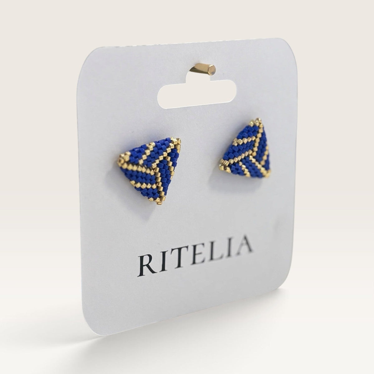 Ritelia handmade triangular stud earrings featuring cobalt blue and gold Miyuki Japanese beads on a display card.