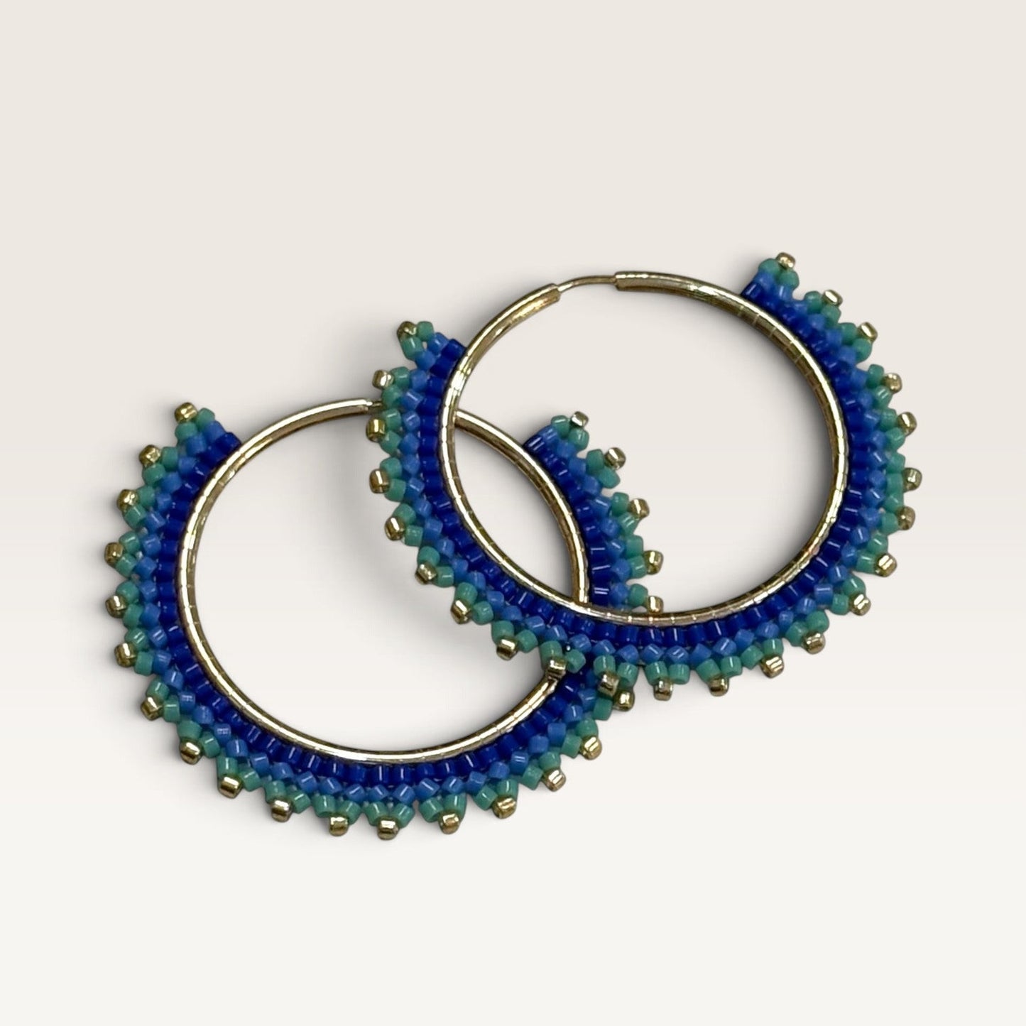Ritelia Abril hoop earrings featuring hand-woven cobalt blue, aqua green, and gold Miyuki beads on gold-plated hoops.