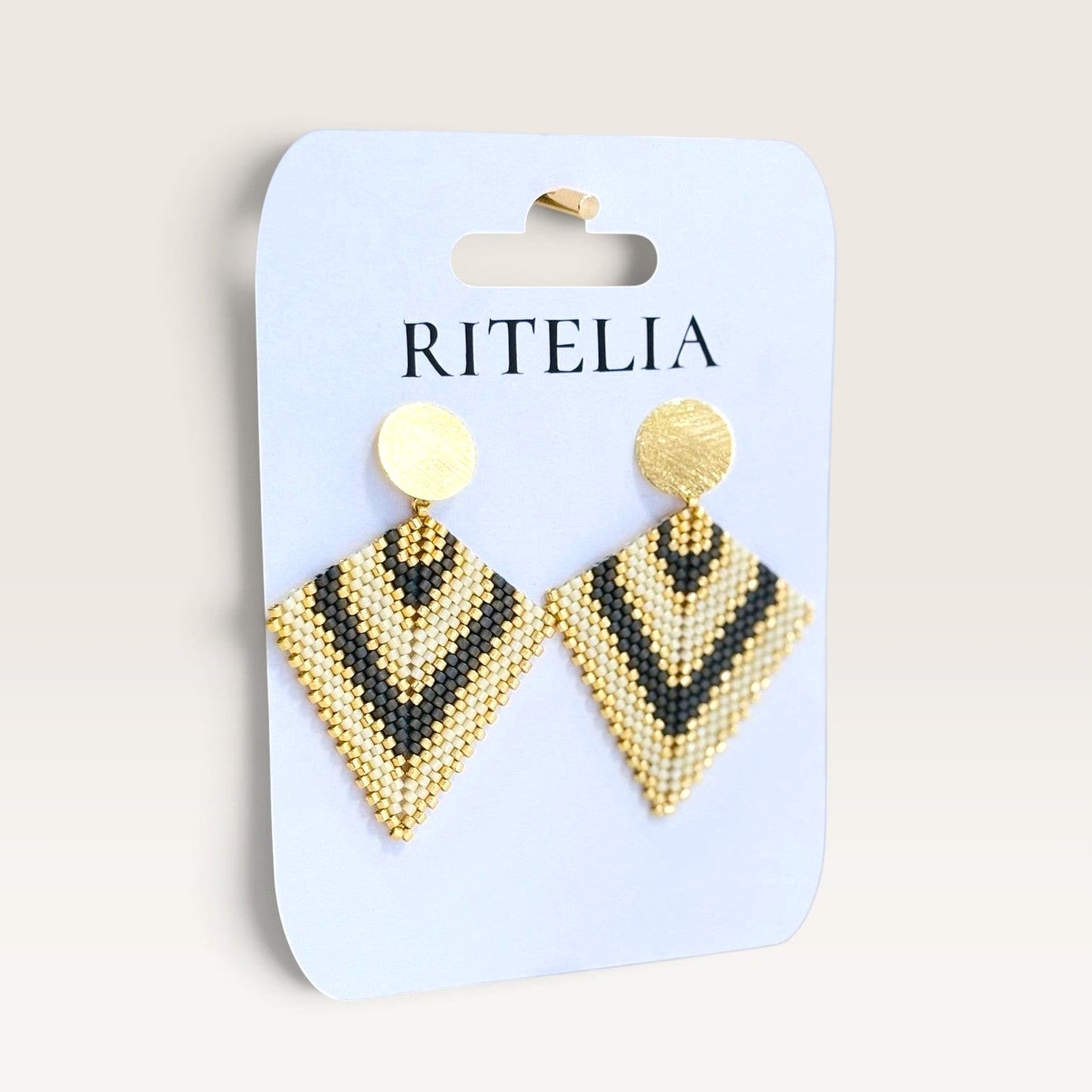 Ritelia Regina handmade diamond-shaped drop earrings with black, cream, and gold Miyuki beads and matte gold studs.