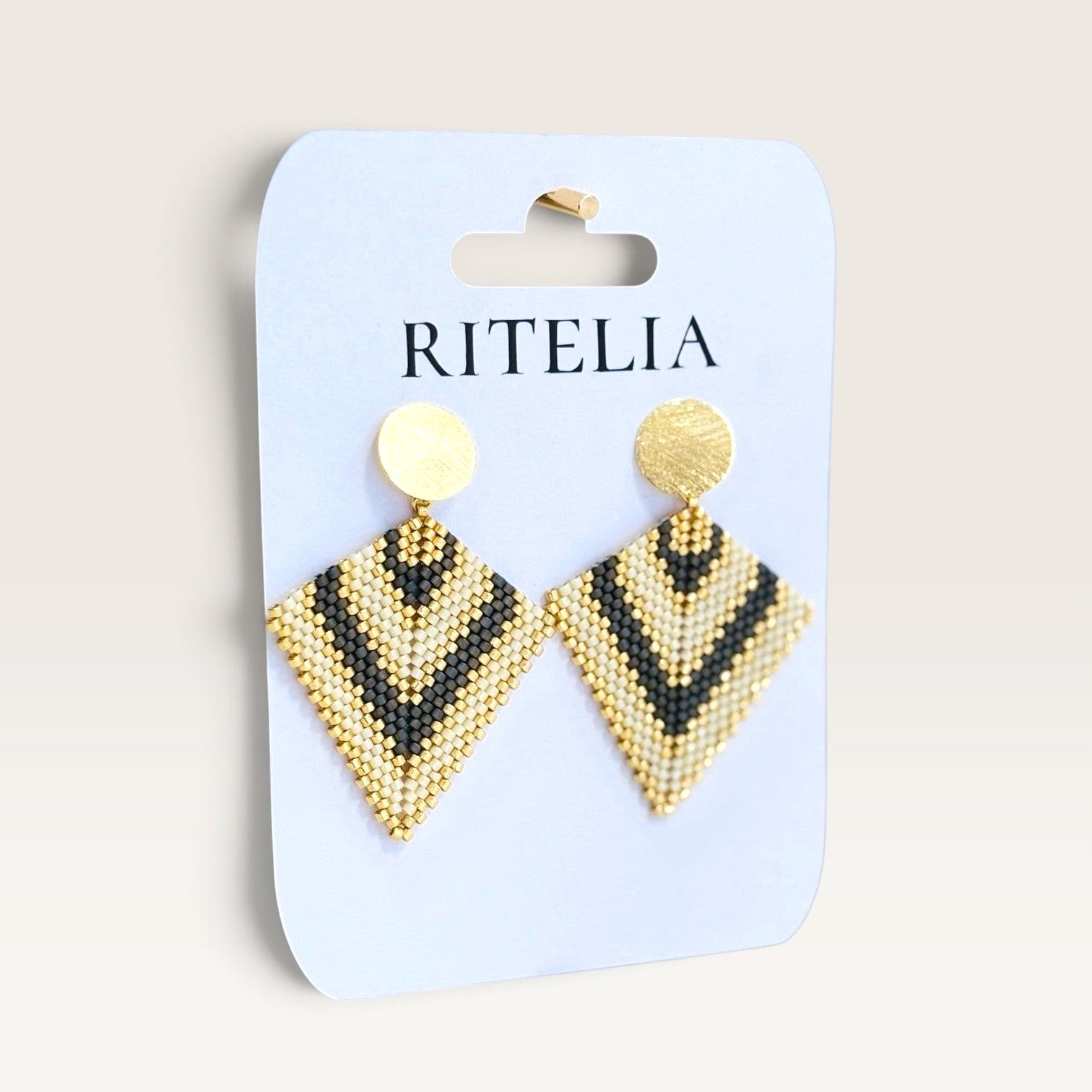 Ritelia Regina handmade diamond-shaped drop earrings with black, cream, and gold Miyuki beads and matte gold studs.